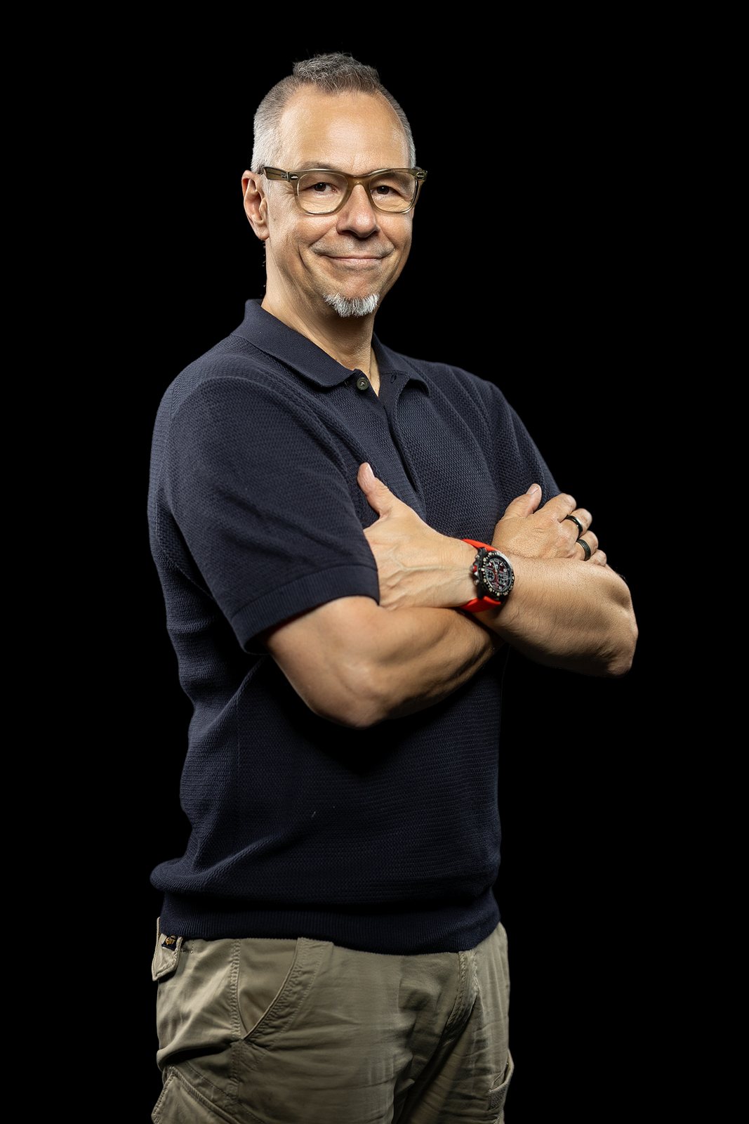 Andreas Schmitt im dunklen Polo mit verschränkten Armen vor schwarzem Hintergrund