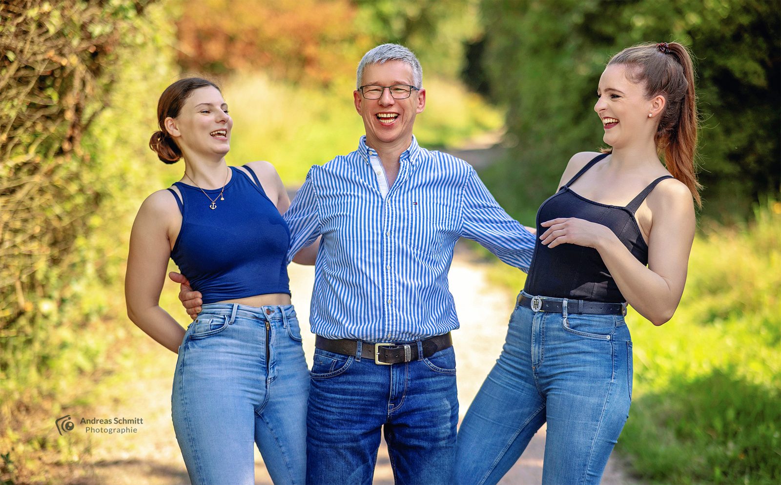 Vater mit zwei erwachsenen Töchtern lacht im Grünen