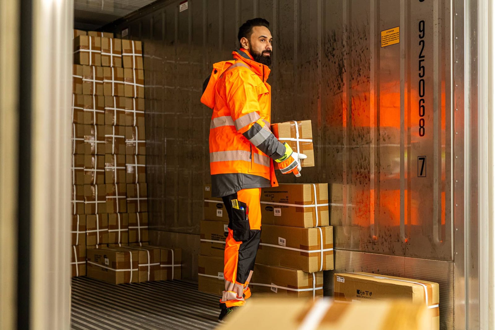 Mitarbeiter in Warnkleidung trägt Pakete aus einem Container