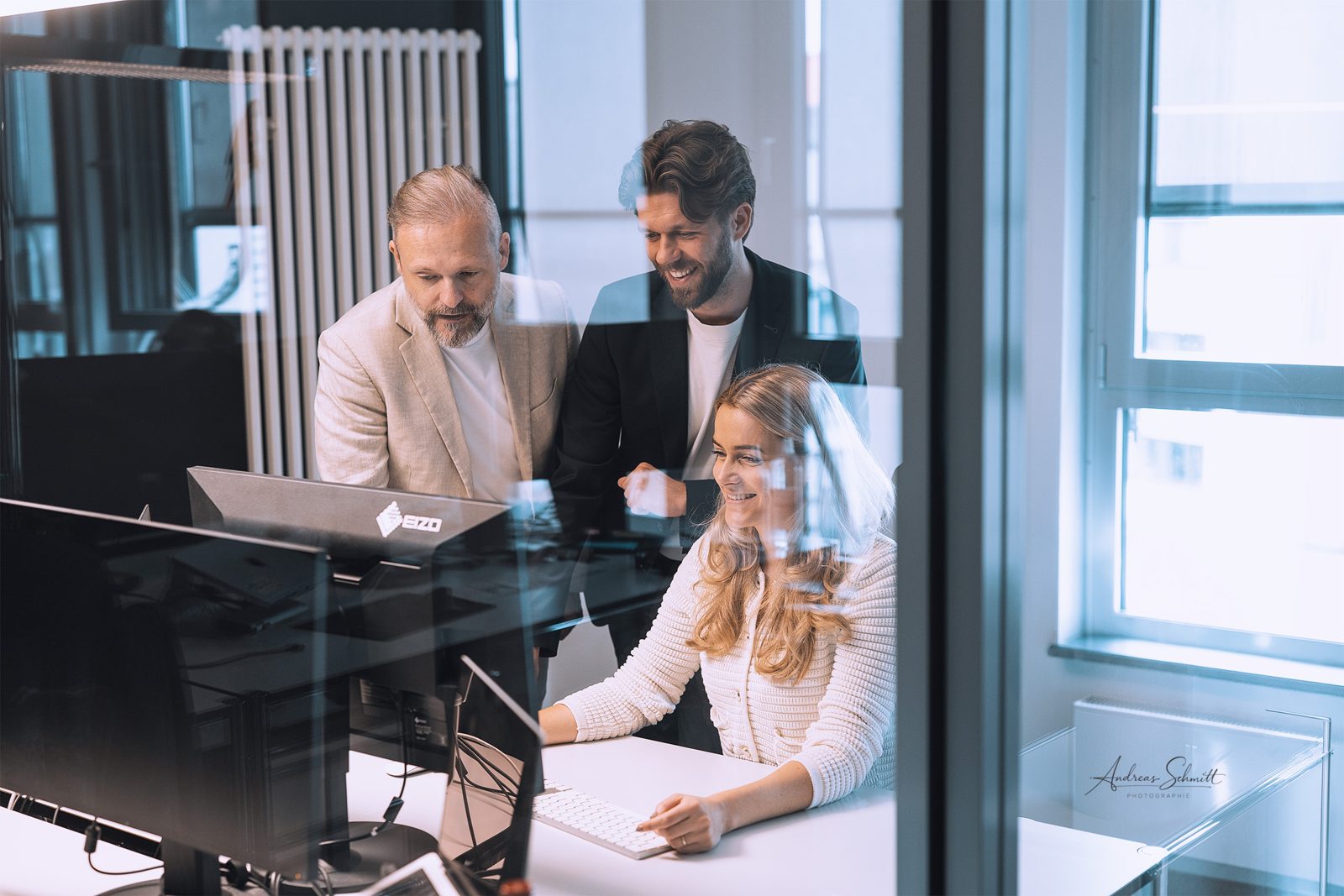 Teamfoto: drei Kollegen besprechen sich am Bildschirm im hellen Büro